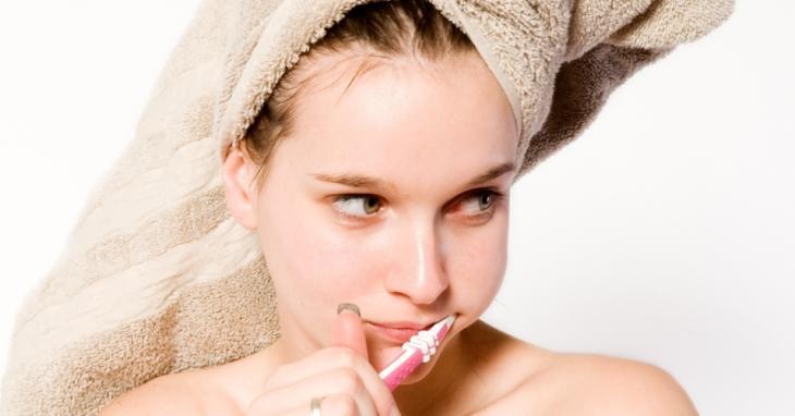 Imagem de uma mulher com uma toalha na cabeça enquanto escova os dentes