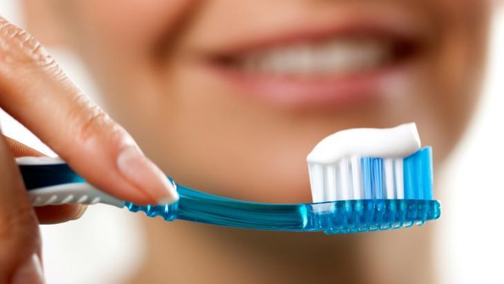 Close de uma escova de dentes, com um sorriso feminino ao fundo