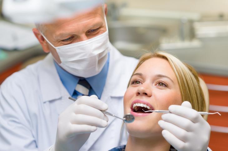 Imagem de dentista examinando paciente em consulta, destacando as fases da vida em que é indicado o implante dentário