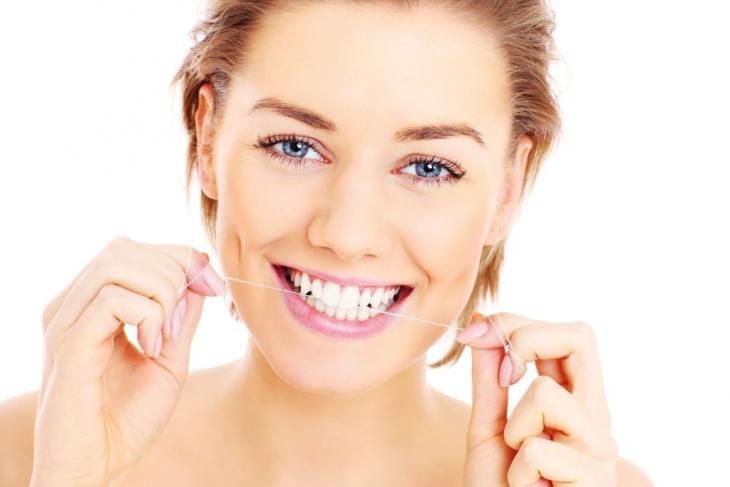 Imagem de uma jovem sorrindo enquanto utiliza fio dental, indicando a sua importância para a higiene bucal