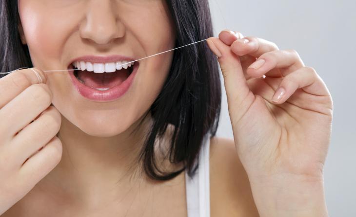 Close de uma boca feminina sorrindo e passando o fio dental