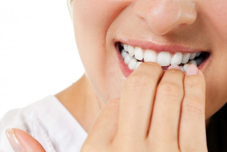 Close de uma boca feminina roendo as próprias unhas