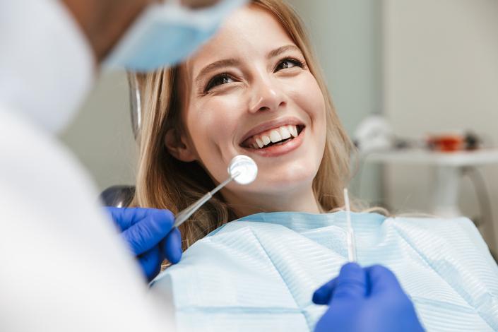Imagem de uma mulher sorrindo durante consulta odontológica, simbolizando a importância de cuidar da saúde bucal
