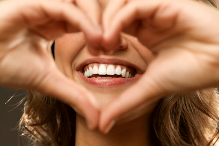 Imagem de uma mulher fazendo o sinal do coração com as mãos e um close em seu sorriso