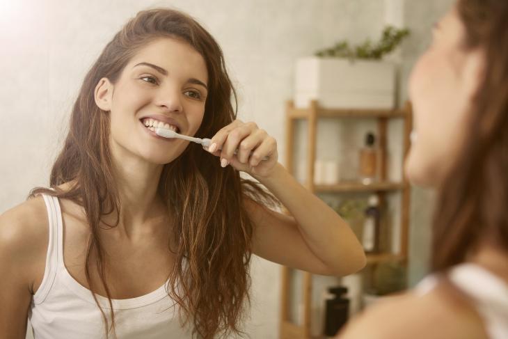 Imagem de uma mulher escovando os dentes em frente a um espelho
