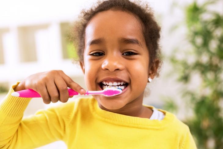 Imagem de uma criança sorrindo enquanto escova os dentes, destacando sua importância para a sensibilidade nos dentes de leite