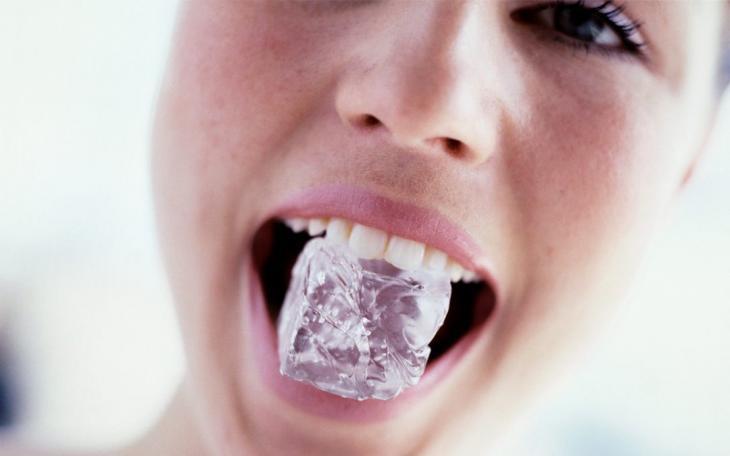 Imagem de uma mulher mordendo cubo de gelo, destacando que mastigar gelo traz danos aos dentes