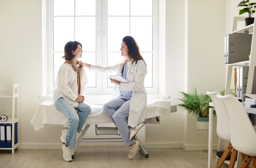 Profissional de saúde conversando e com a mão no ombro de mulher jovem, simbolizando avaliação óssea e prevenção da osteopenia precoce.