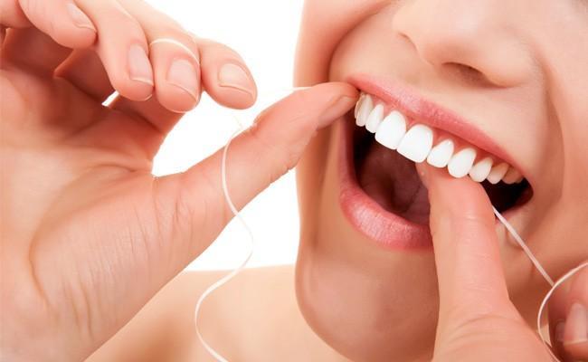 Imagem de uma pessoa usando fio dental para remover a placa bacteriana, indicando a importância da higiene bucal