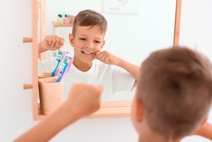 Imagem de um menino utilizando o fio dental, indicando a introdução do uso do fio dental na rotina de uma criança