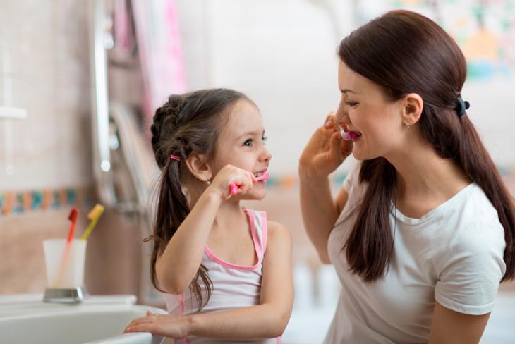 Imagem de uma mãe e filha escovando os dentes juntas, simbolizando o estímulo a escovar os dentes desde cedo