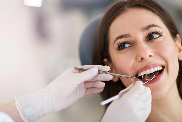 Imagem de uma mulher sorrindo durante consulta odontológica, enquanto dentista examina seus dentes.