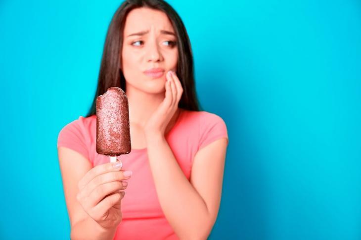 Imagem de uma mulher segurando um sorvete com uma mão e a outra na bochecha, indicando incômodo
