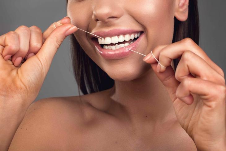 Imagem de uma mulher sorridente usando fio dental para manter a higiene bucal e a saúde dos dentes