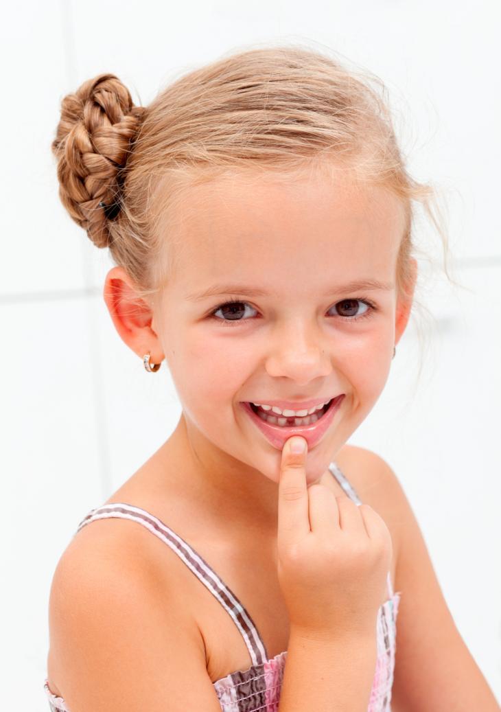 Imagem de uma menina apontando para um dente de leite que caiu, representando a extração de dentes na fase de troca dentária
