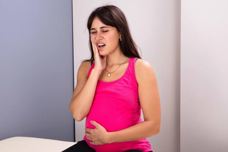 Imagem de uma mlher grávida com uma mão na barriga e a outra na bochecha, indicando dor