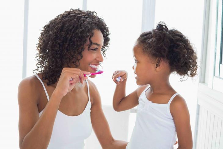 Imagem de uma mulher e uma criança se olhando frente a frente enquanto escovam os dentes
