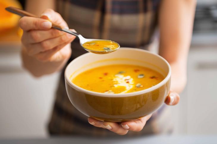 Close de mãos femininas segurando um pote de sopa