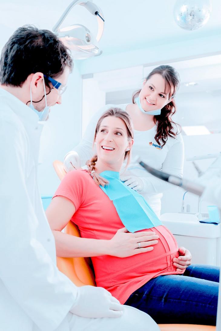 Imagem de uma mulher sorrindo em uma consulta odontológica enquanto está acompanhada de dois profissionais da área