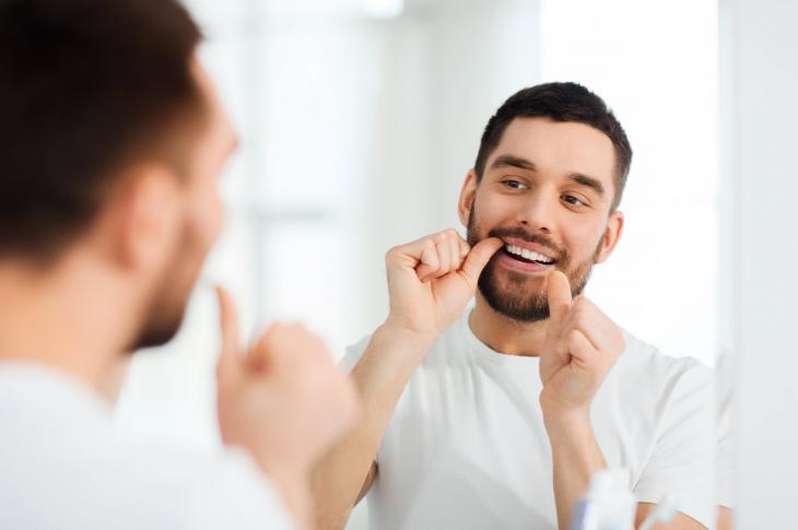 Imagem de uma homem passando o fio dental em frente a um espelho
