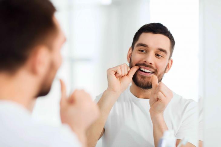 Imagem de uma homem passando o fio dental em frente a um espelho