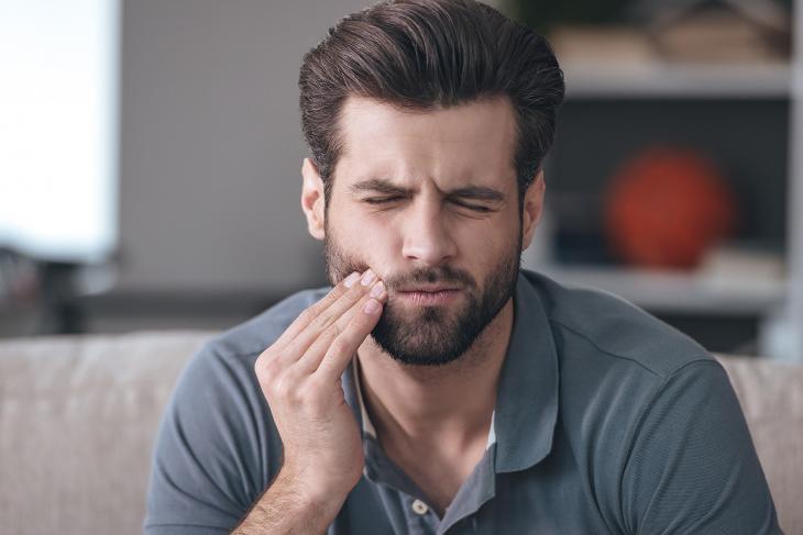 Imagem de um homem com a mão na bochecha e uma feição de dor