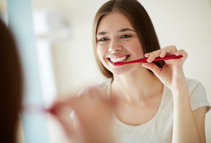 Imagem de uma mulher escovando os dentes em frente a um espelho