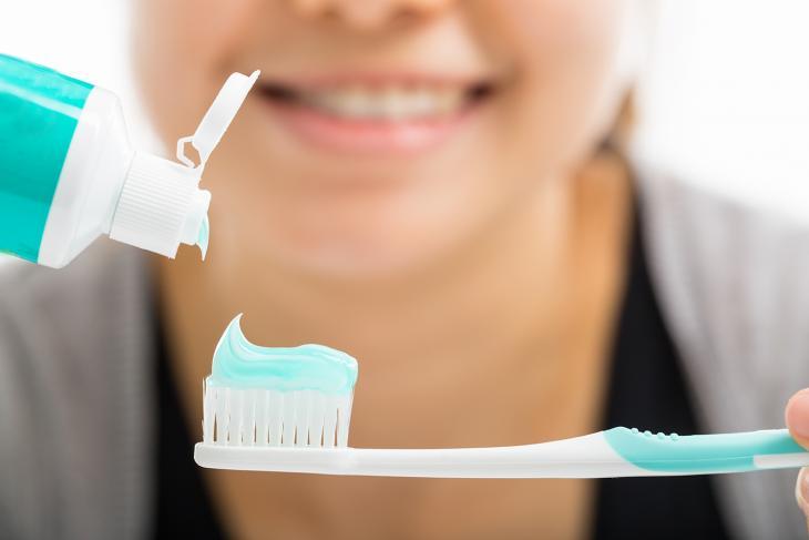 Imagem de uma jovem sorrindo enquanto aplica creme dental em uma escova de dentes, destacando a importância da higiene bucal