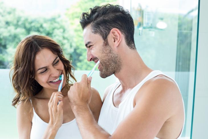 Imagem de um casal sorrindo enquanto escova os dentes, simbolizando uma higiene bucal adequada