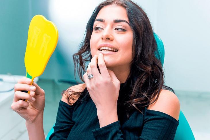 Imagem de uma mulher observando os dentes através de um espelho
