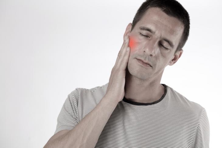 Imagem de um homem tocando o rosto com dor, indicando inflamação ao redor de um implante dentário, como peri-implantite