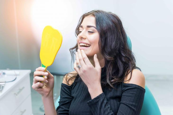 Imagem de uma mulher observando os dentes através de um espelho