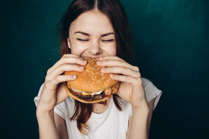 Imagem de uma mulher sorrindo enquanto morde um hambúrguer