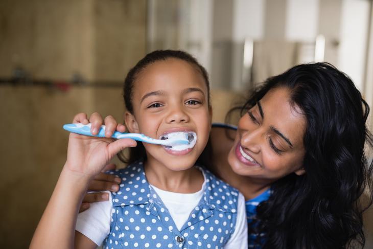 Imagem de uma criança escovando os dentes, acompanhada de sua mãe, destacando a importância dos cuidados com a gengiva