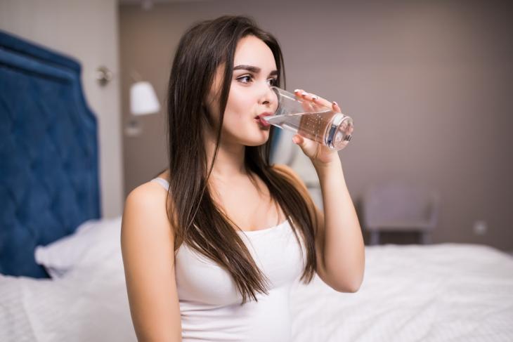 Imagem de uma mulher tomando água em um copo de vidro transparente, indicando que a boca seca precisa de cuidados