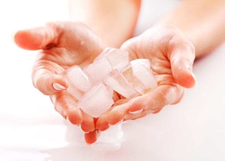Imagem de mãos segurando cubos de gelo. Mastigar gelo pode causar sensibilidade, desgaste no esmalte e fraturas nos dentes
