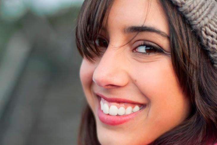 Imagem de uma jovem sorrindo, de forma tímida, indicando como o sorriso gengival pode afetar a auto estima