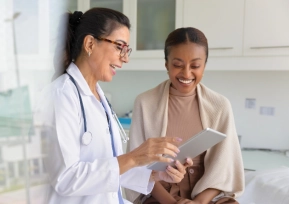 Médica da rede Hapvida orientando paciente durante consulta clínica, analisando informações em tablet em ambiente hospitalar moderno.