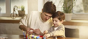 Pai e filho montando um brinquedo em cima da mesa.