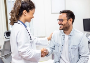 Médica cumprimenta paciente sorridente em consultório, representando atendimento humanizado.
